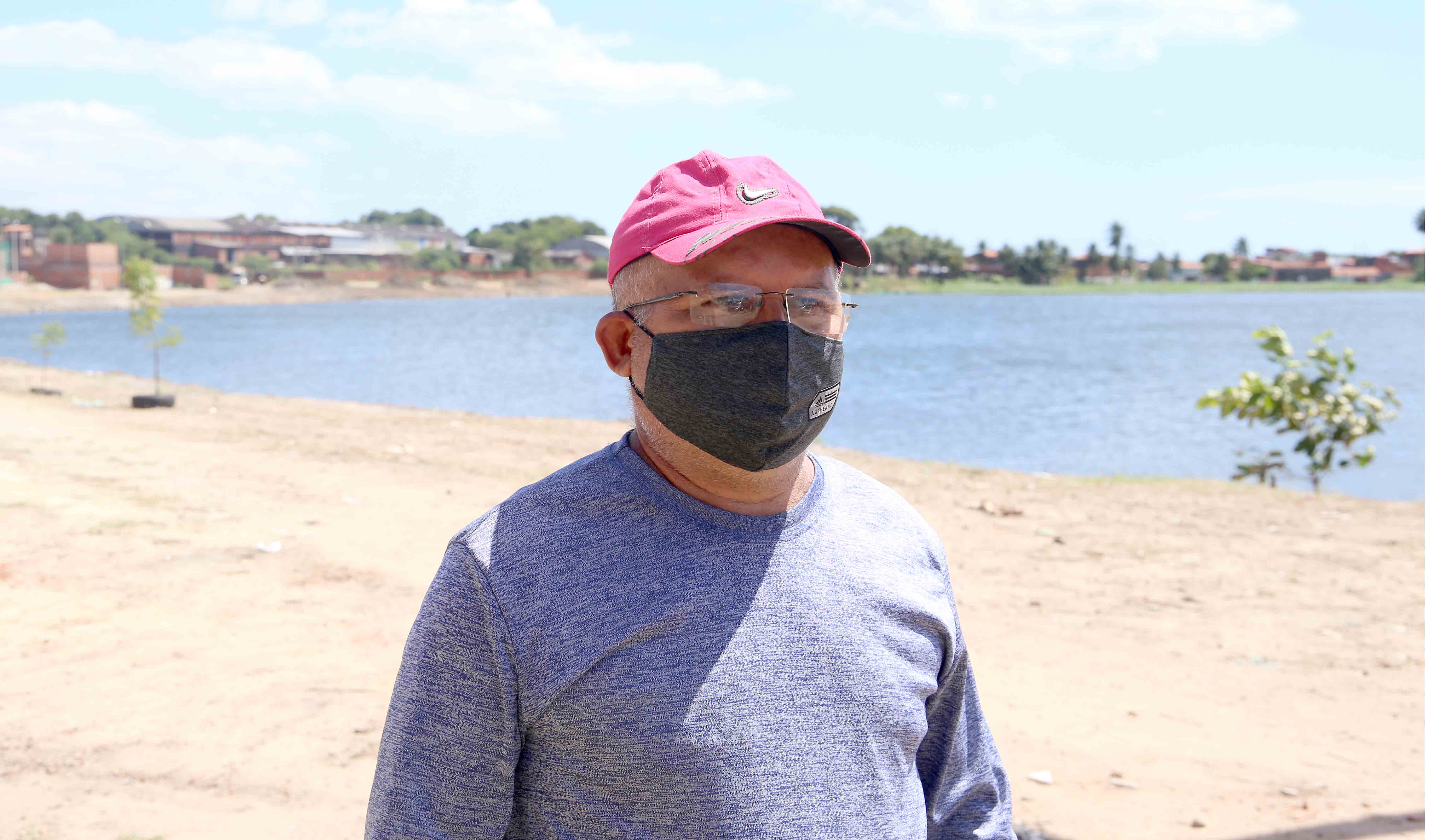 senhor de boné e máscara posando para a foto com Lagoa do Urubu ao fundo